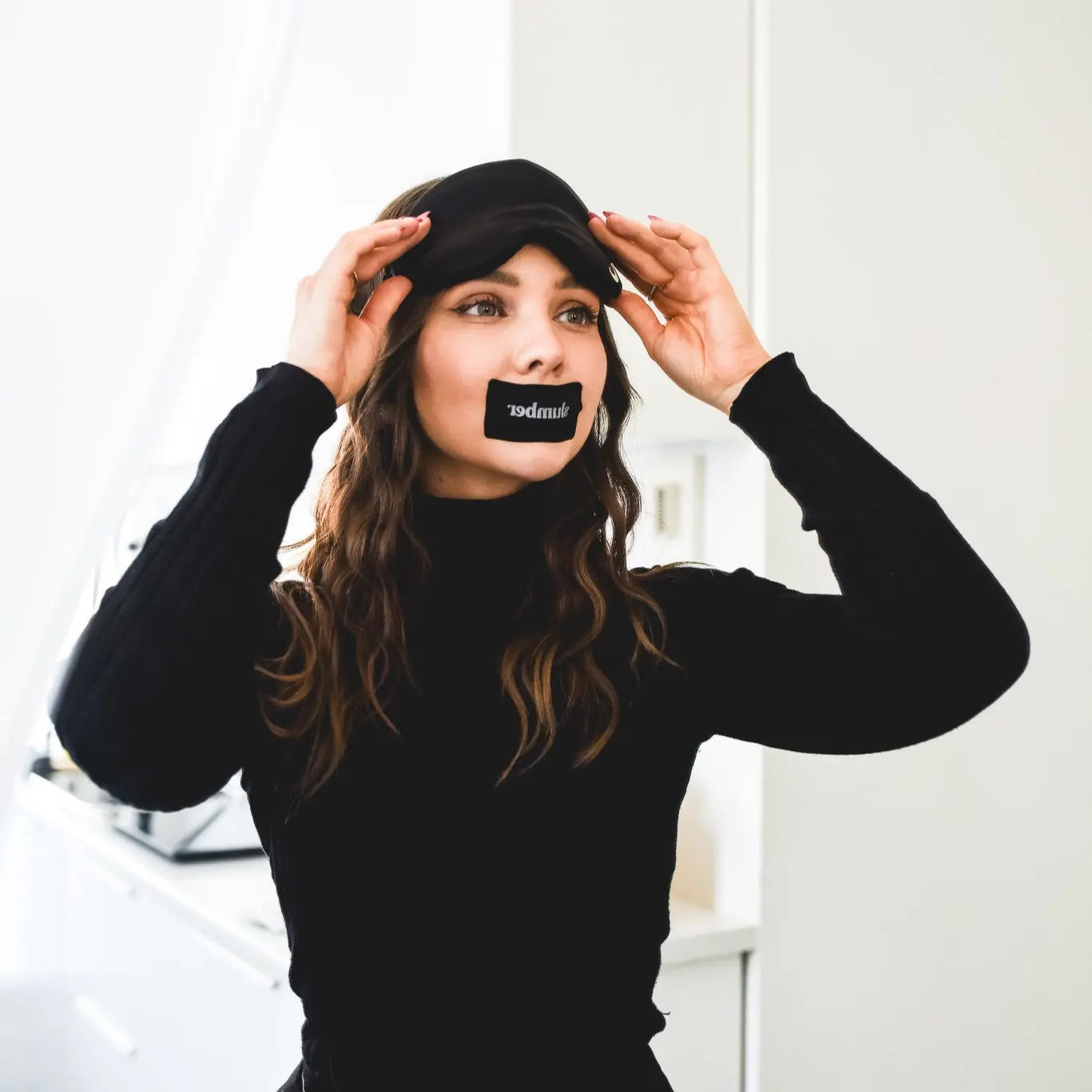 Woman wearing a Slumber sleep mask and mouth tape, preparing for better sleep in a modern, well-lit room.